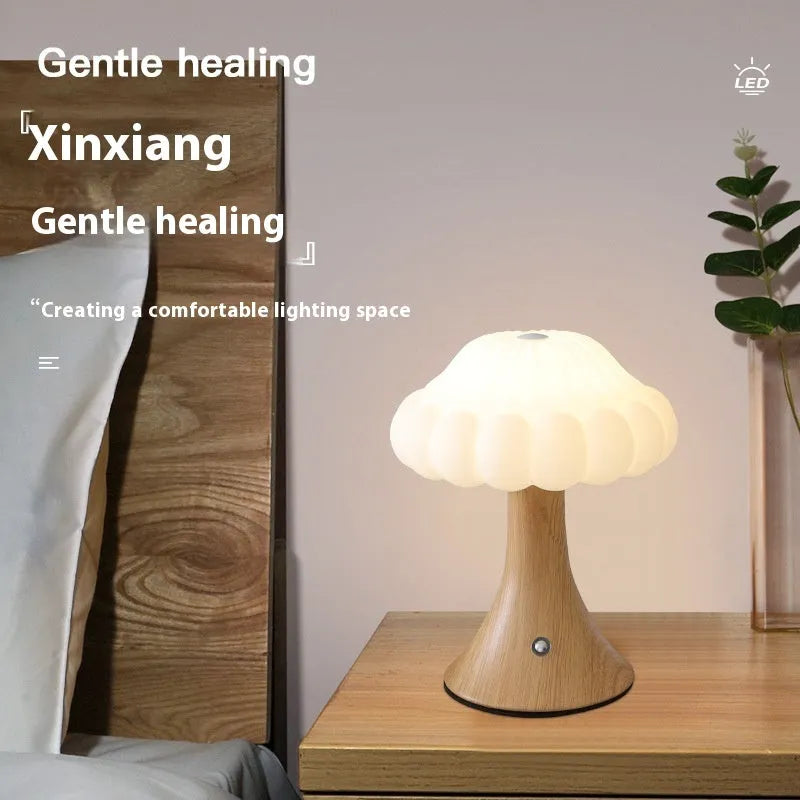 Small mushroom-shaped touch night lamp in wood grain colour on a table.