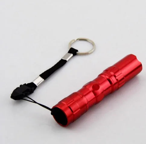 Black aluminium mini LED flashlight on a dark background, shown with AA battery for scale.