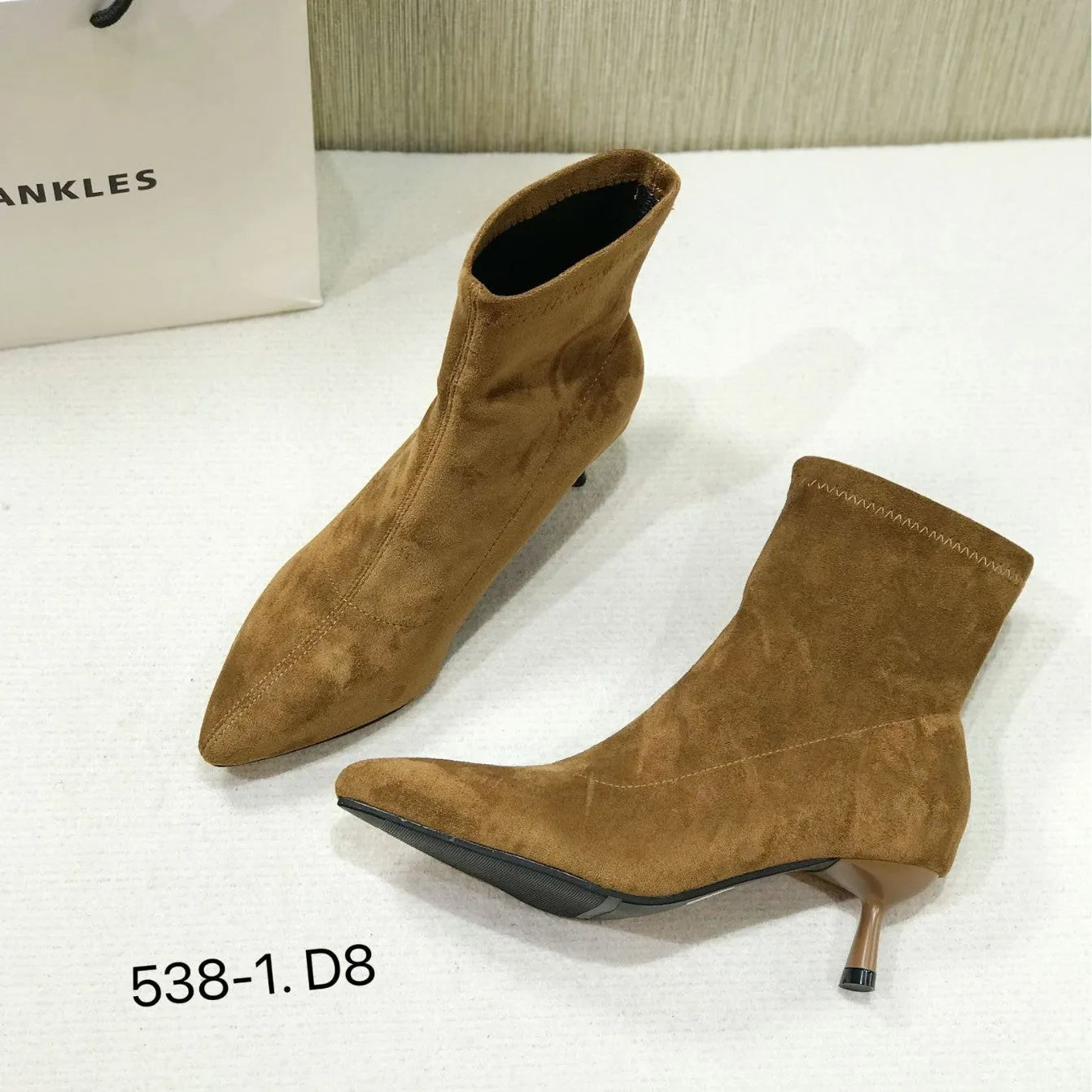 Black pointed toe stiletto ankle boots with a mid-calf sock on a plain background.