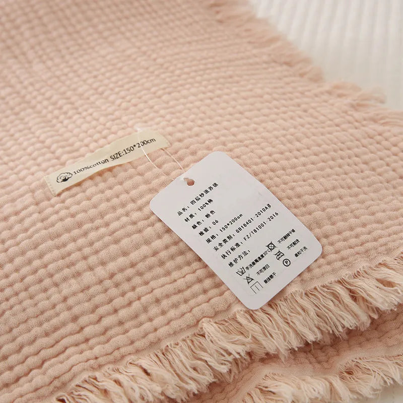 Four-layer gauze cotton tassel blanket in avocado green colour laid flat.