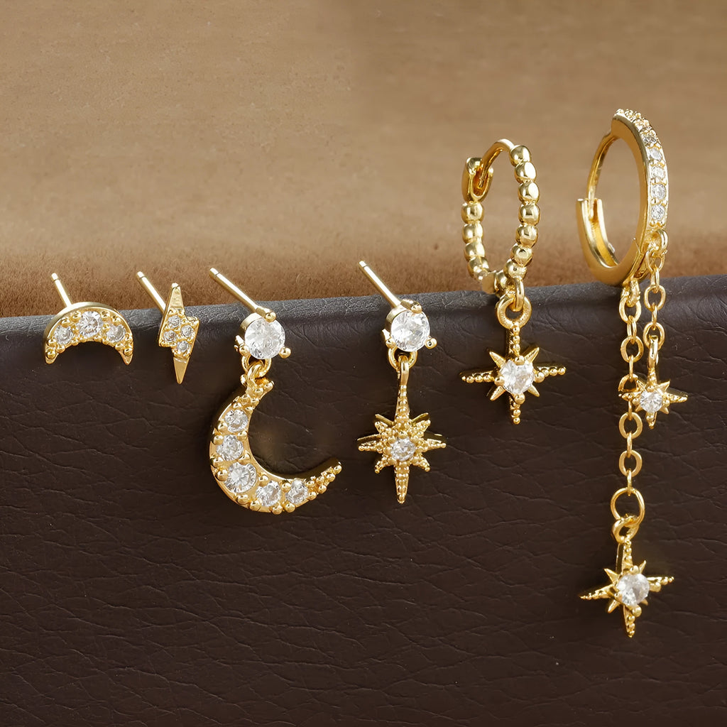 Set of six pairs of gold chain tassel drop earrings with zircon studs laid out on a surface.