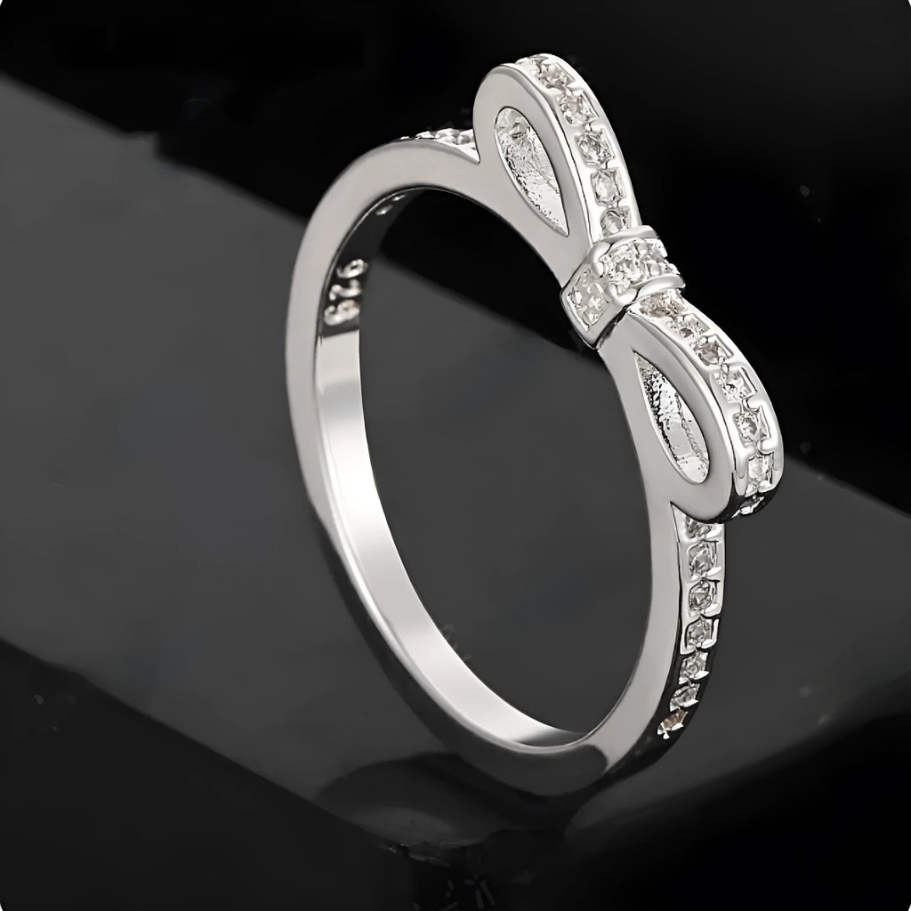 A silver-coloured bow-shaped ring set with sparkling clear rhinestone crystals on a finger.