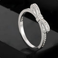 A silver-coloured bow-shaped ring set with sparkling clear rhinestone crystals on a finger.