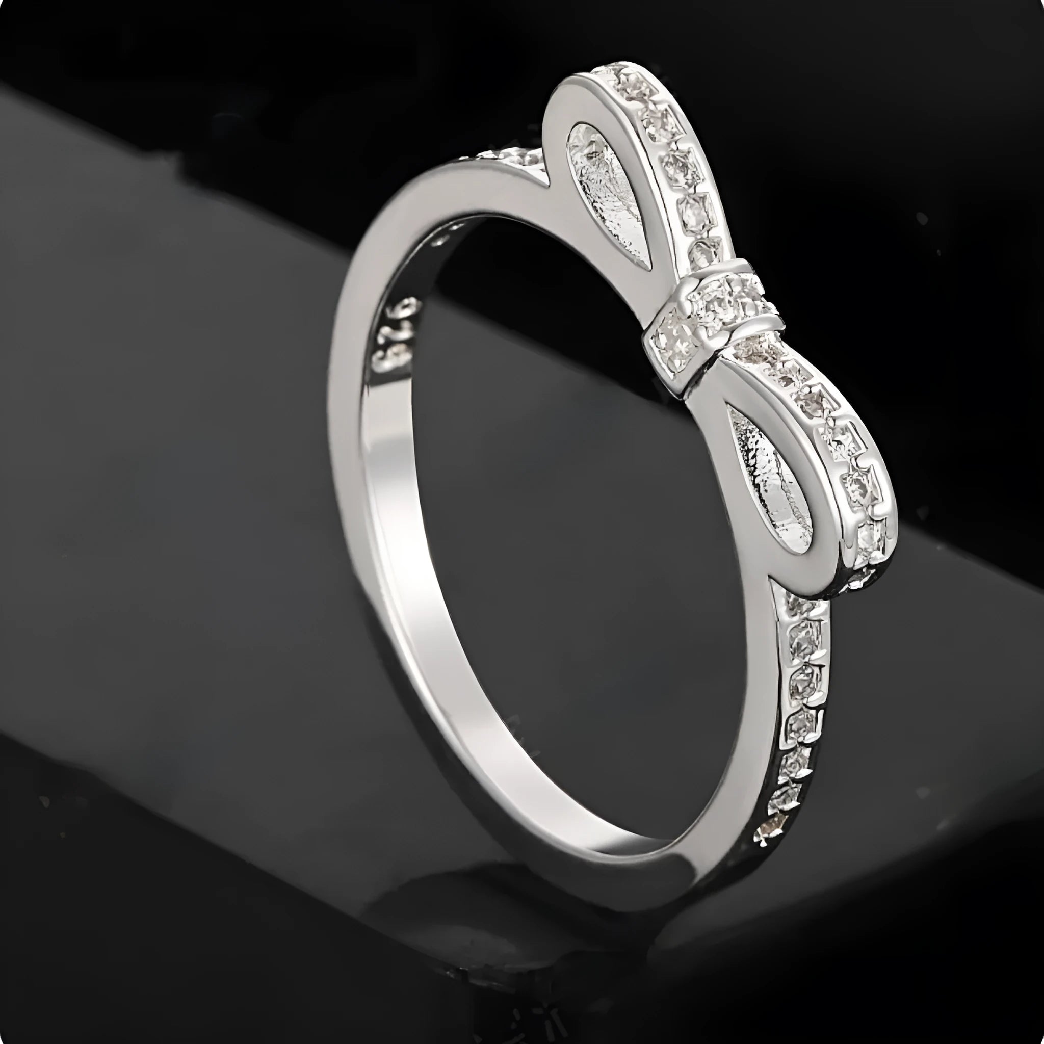 A silver-coloured bow-shaped ring set with sparkling clear rhinestone crystals on a finger.