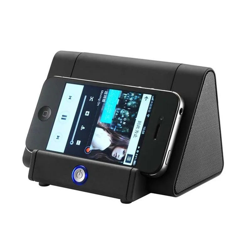 Small black or white wireless Bluetooth speaker with built-in charging cable on a desk next to a mobile phone
