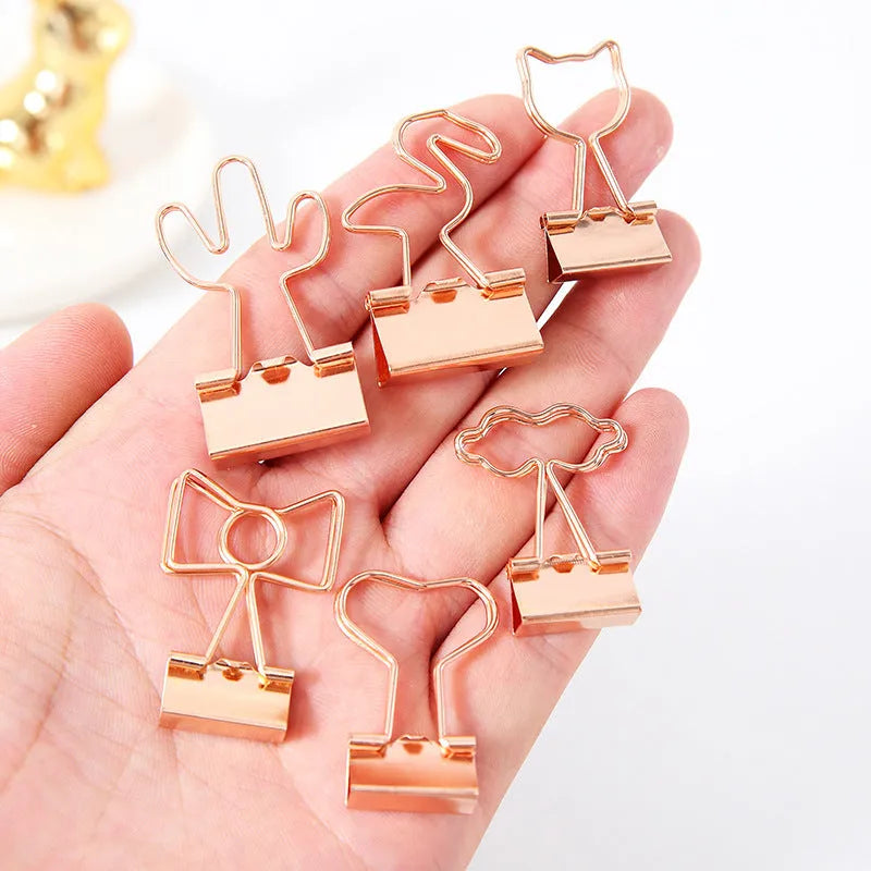 Small gold-plated metal stationery clip with a decorative bow charm design.