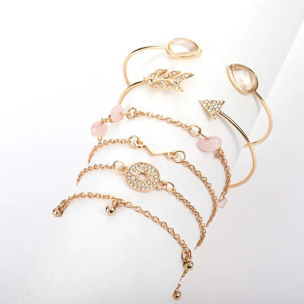 Set of six gold bracelets with arrow, V-shape, and water droplet charms on a dark background.
