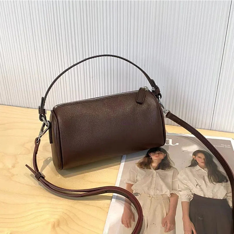 Brown cylindrical leather crossbody phone bag with visible stitching on a flat surface.