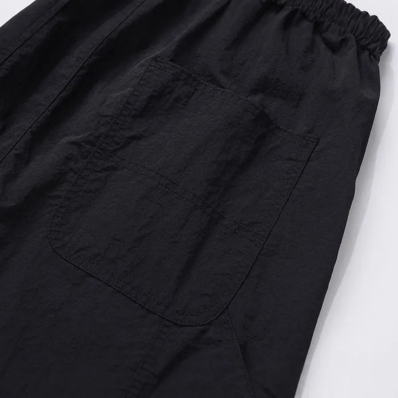Men's black baggy paratrooper pants with a drawstring waist on a neutral background.