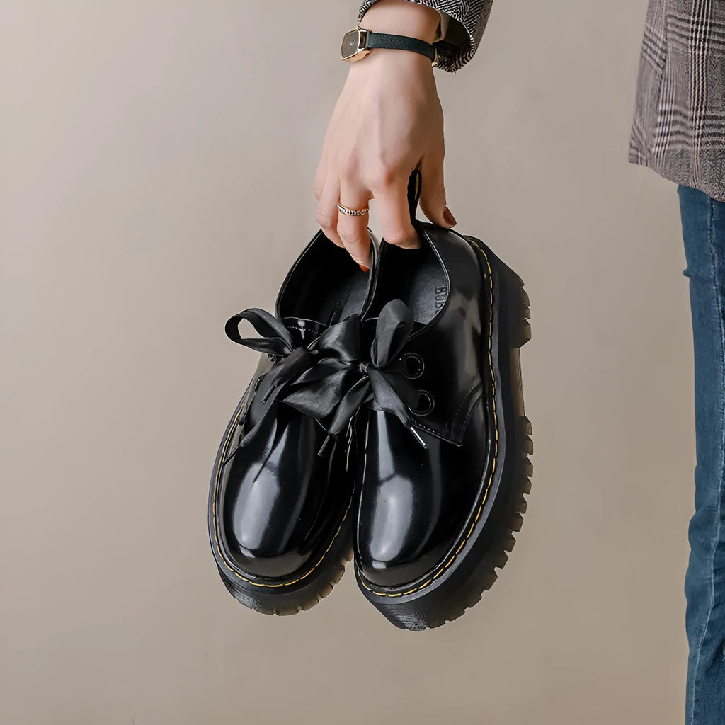 Women's white and black leather shoes with thick soles, ribbon and cross-strap design, and laced closure.