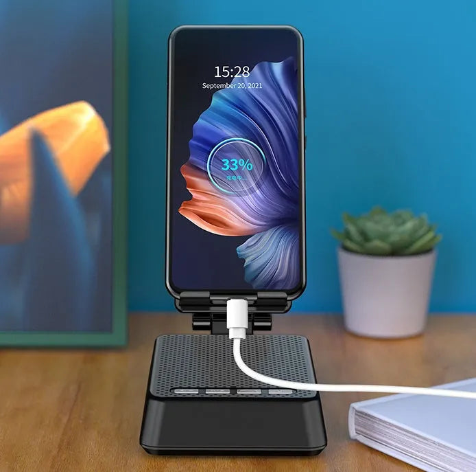 Black mobile phone broadcasting stand with integrated Bluetooth speaker on a desk.
