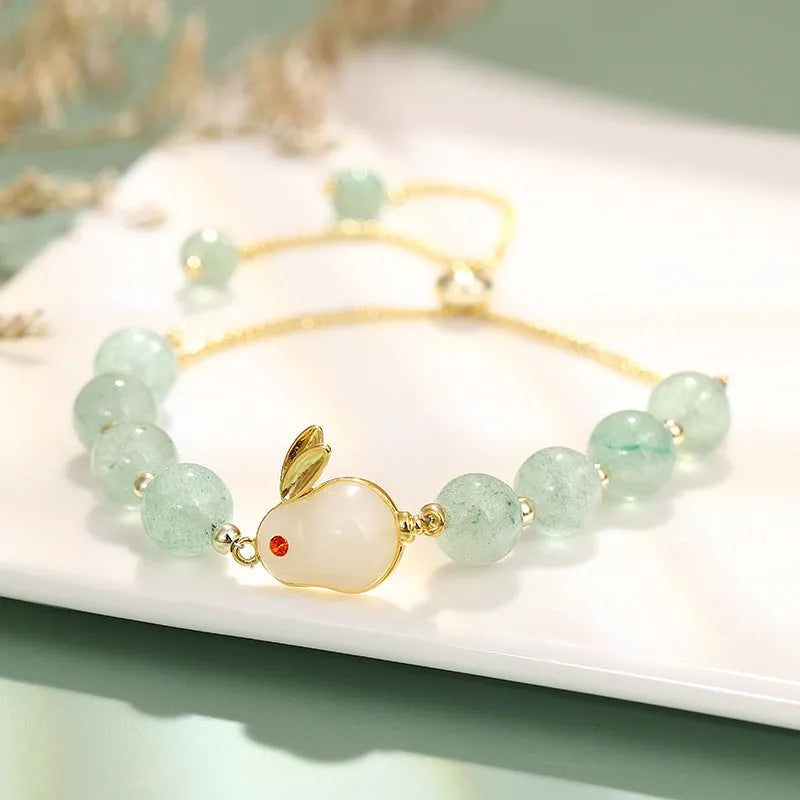 Rabbit charm bracelet with green aventurine or strawberry quartz stones and gold accents on a wrist.