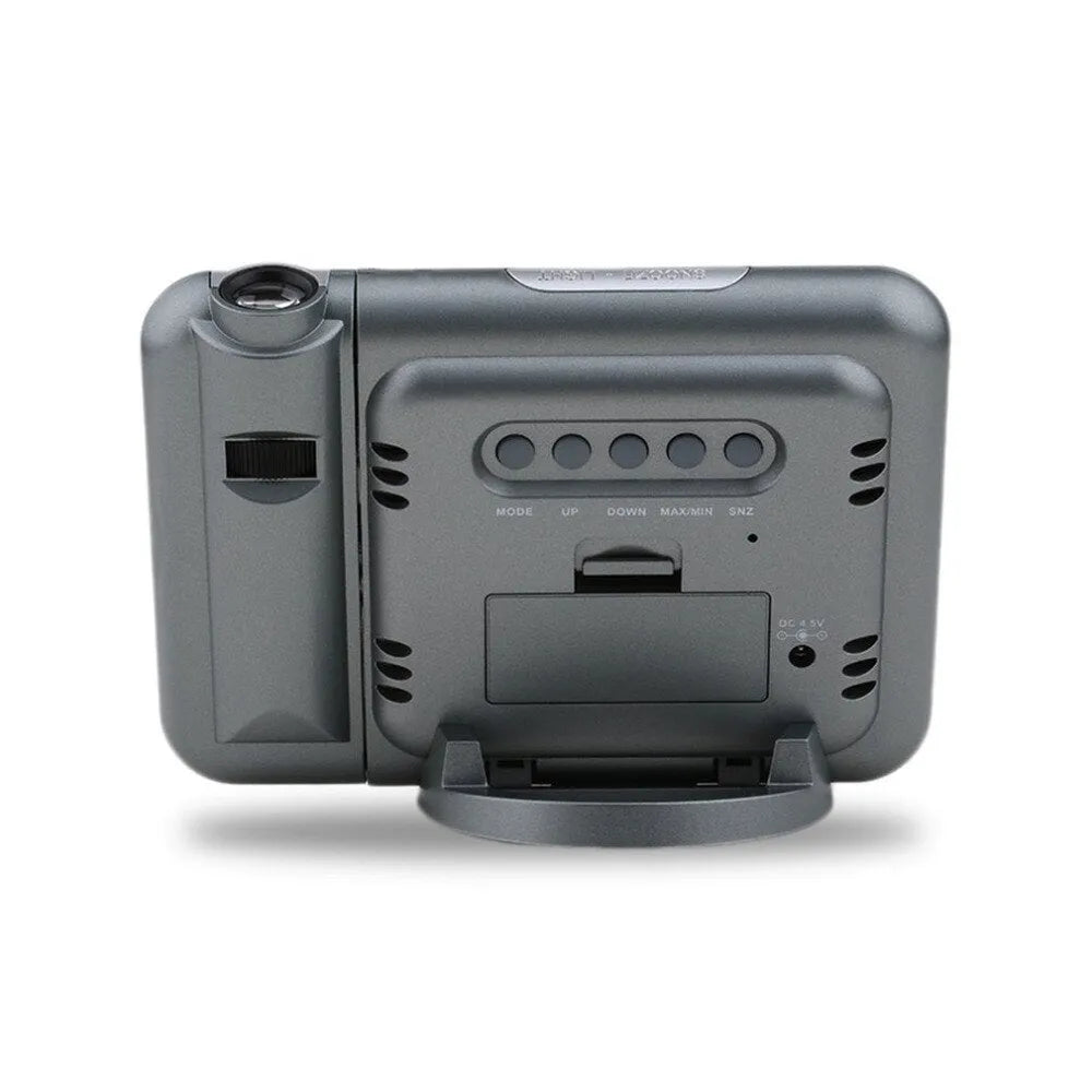 Black digital projection alarm clock with multicolour LED display on a bedside table.