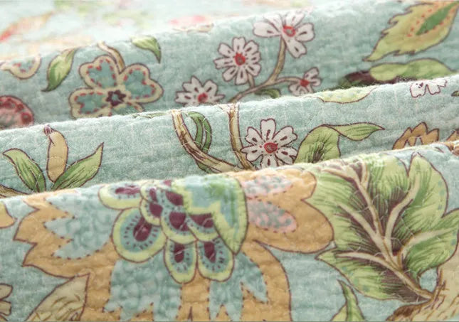 Blue American floral and bird pattern cotton bedspread quilted set of three pieces on a bed.