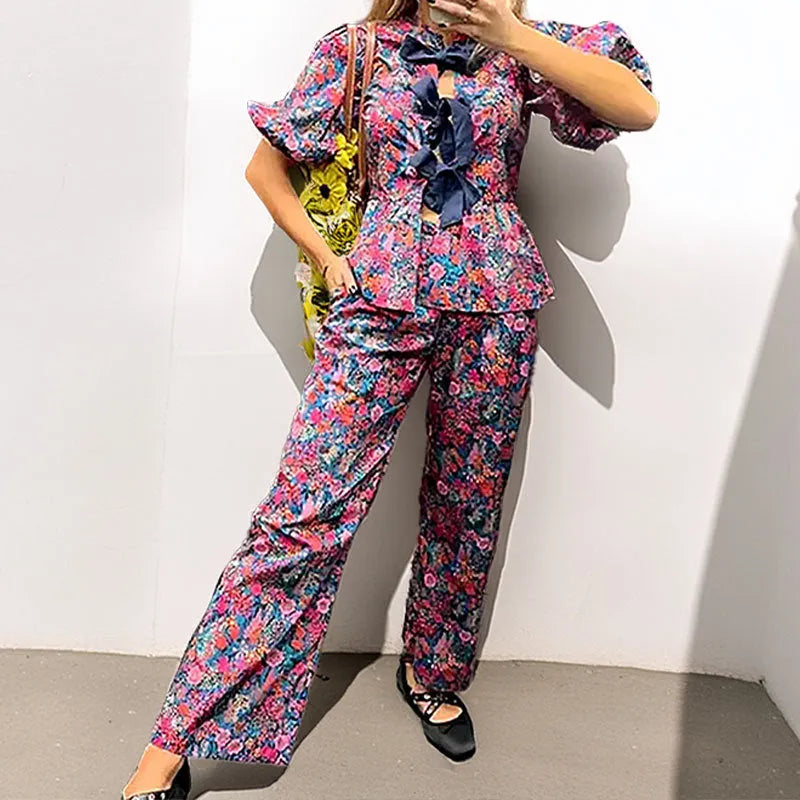 Women's floral print two-piece suit with a tie-neck puff sleeve blouse and straight-leg trousers.