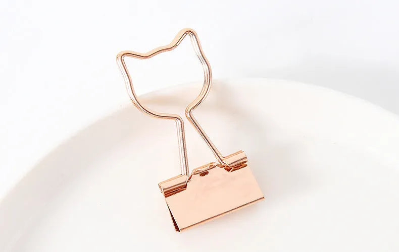 Small gold-plated metal stationery clip with a decorative bow charm design.