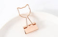 Small gold-plated metal stationery clip with a decorative bow charm design.
