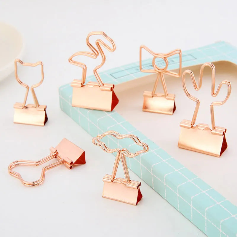 Small gold-plated metal stationery clip with a decorative bow charm design.