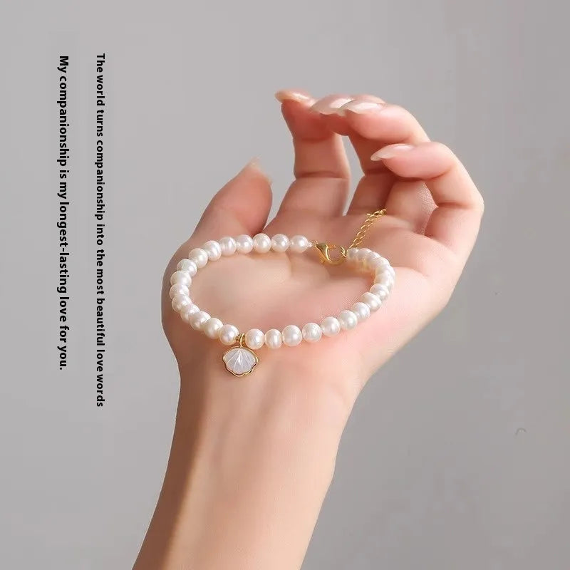 Women's freshwater pearl bracelet with a fan-shaped shell on a wrist, showing elastic and extension chain fastening options.