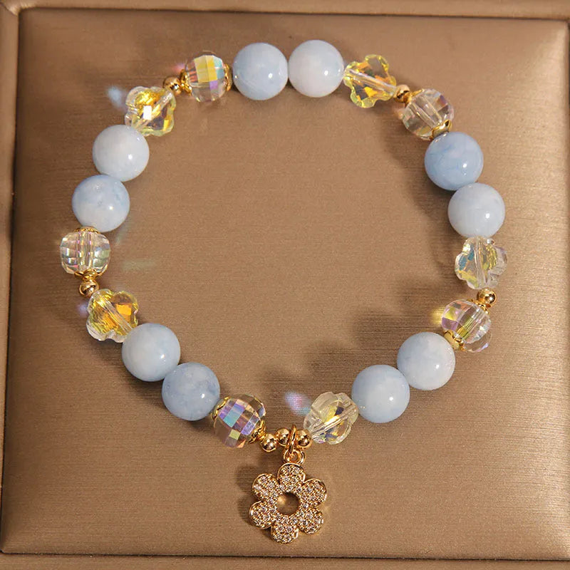 Women's aquamarine crystal bracelet with four-leaf clover charm and pearl details on a wrist.