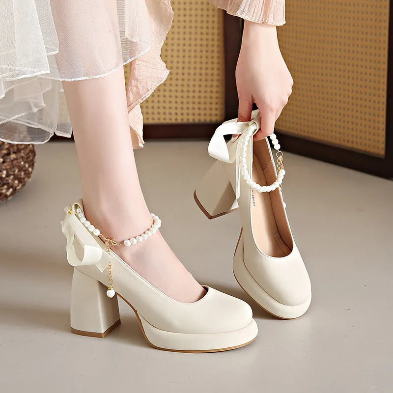 Beige women's Mary Jane shoes with a chunky block heel, ankle strap buckle, and round toe with pearl detail.