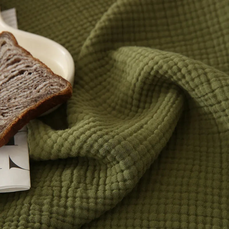 Four-layer gauze cotton tassel blanket in avocado green colour laid flat.