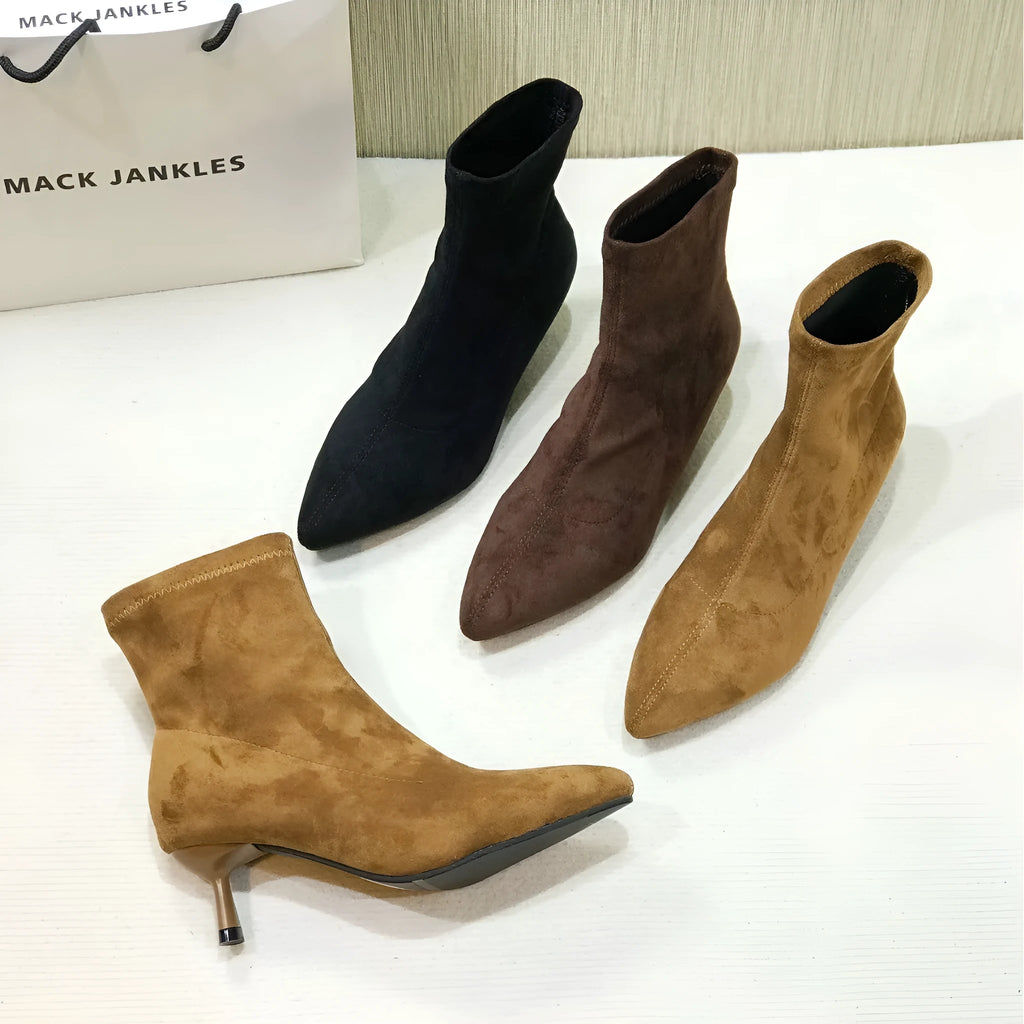 Black pointed toe stiletto ankle boots with a mid-calf sock on a plain background.