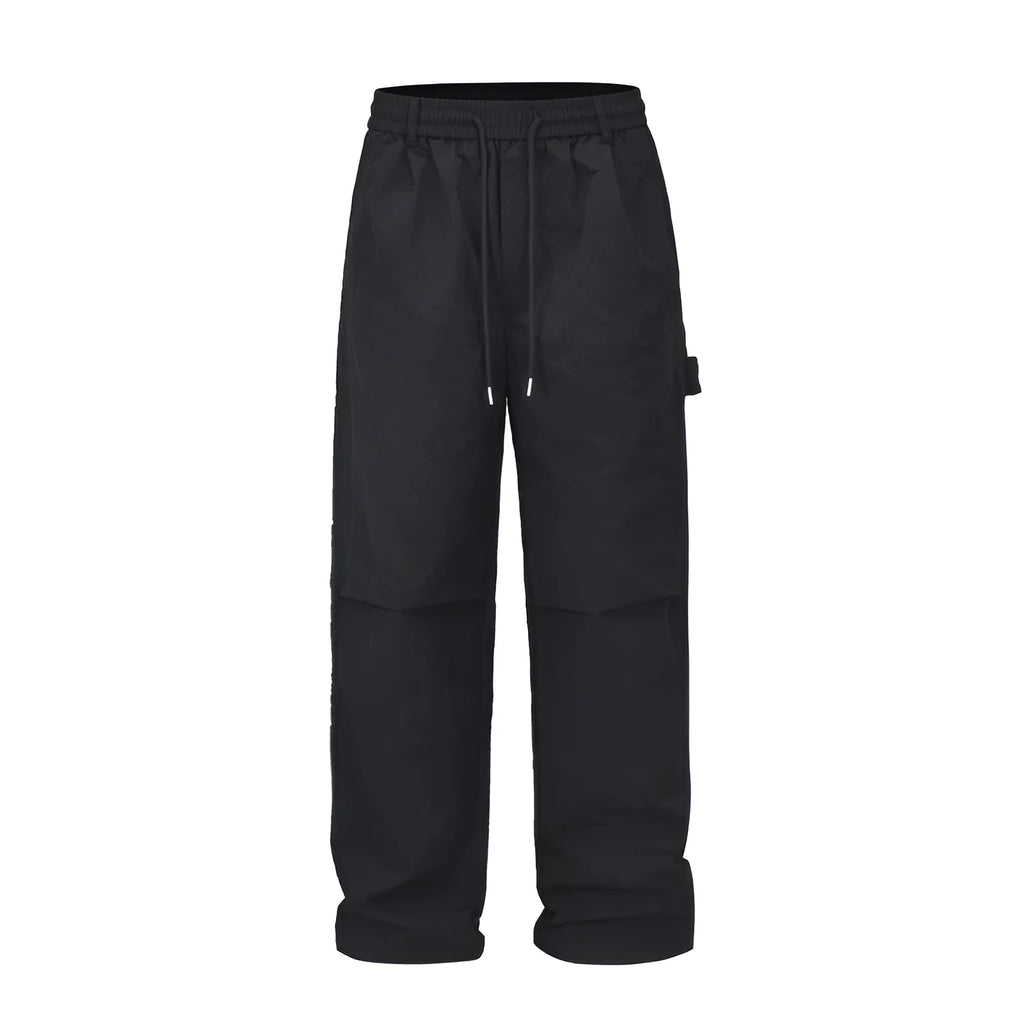 Men's black baggy paratrooper pants with a drawstring waist on a neutral background.