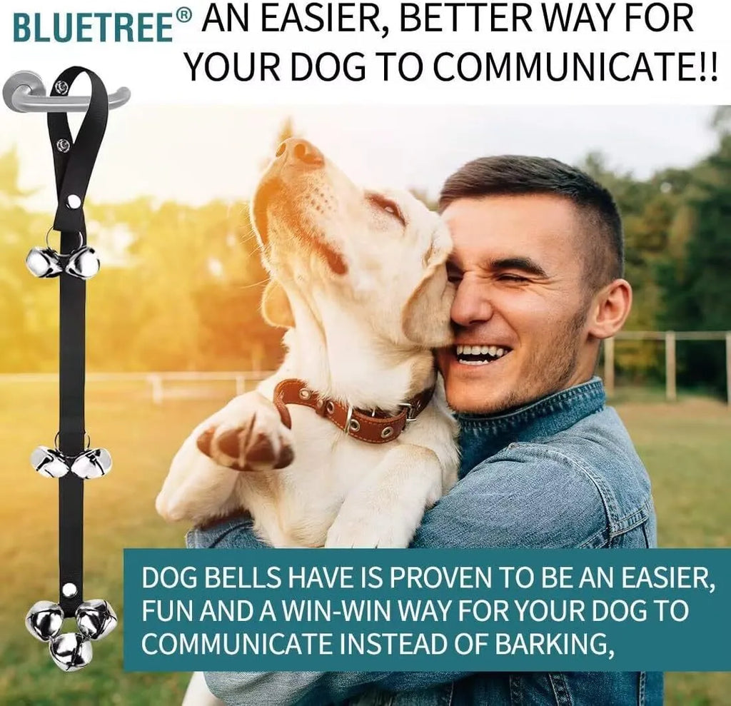 Silver metal dog training bells on an adjustable black nylon leash hanging from a door handle.