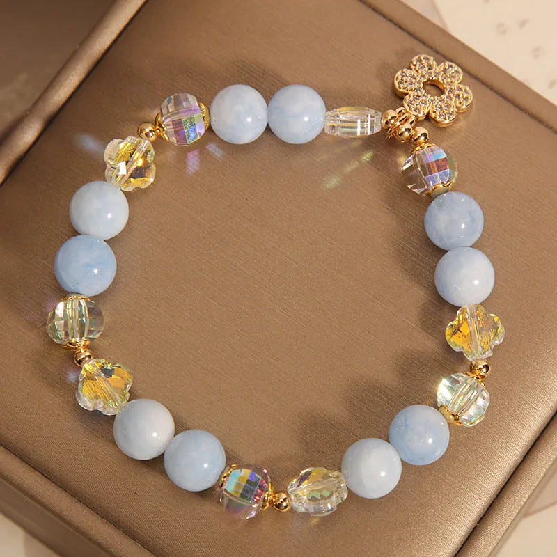 Women's aquamarine crystal bracelet with four-leaf clover charm and pearl details on a wrist.