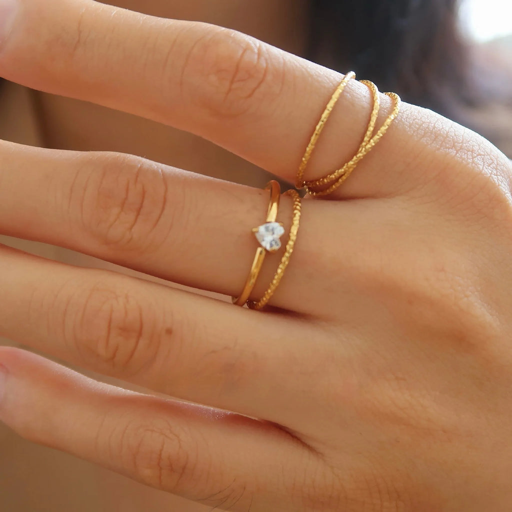 A golden stainless steel ring in a heart shape, shown next to an oval version, on a plain background.