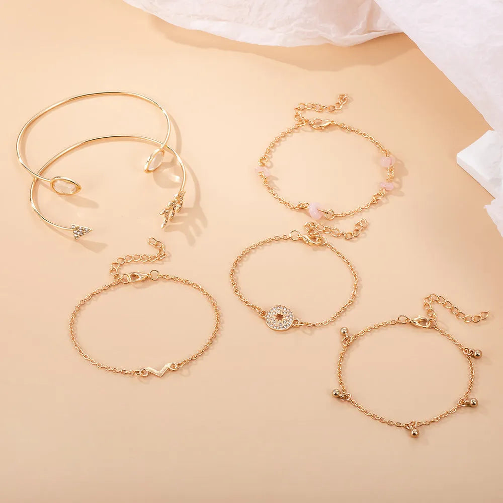 Set of six gold bracelets with arrow, V-shape, and water droplet charms on a dark background.
