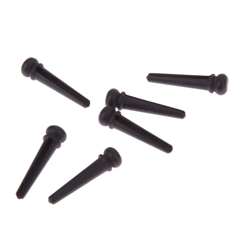 Six matt black ebony guitar string nails for folk acoustic guitars on a white background.
