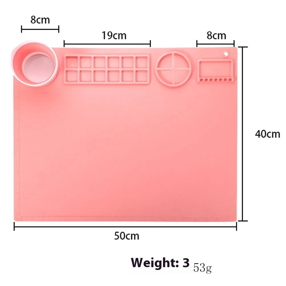 Light blue silicone painting mat with two bowl depressions for water and brushes, placed on a wooden table.