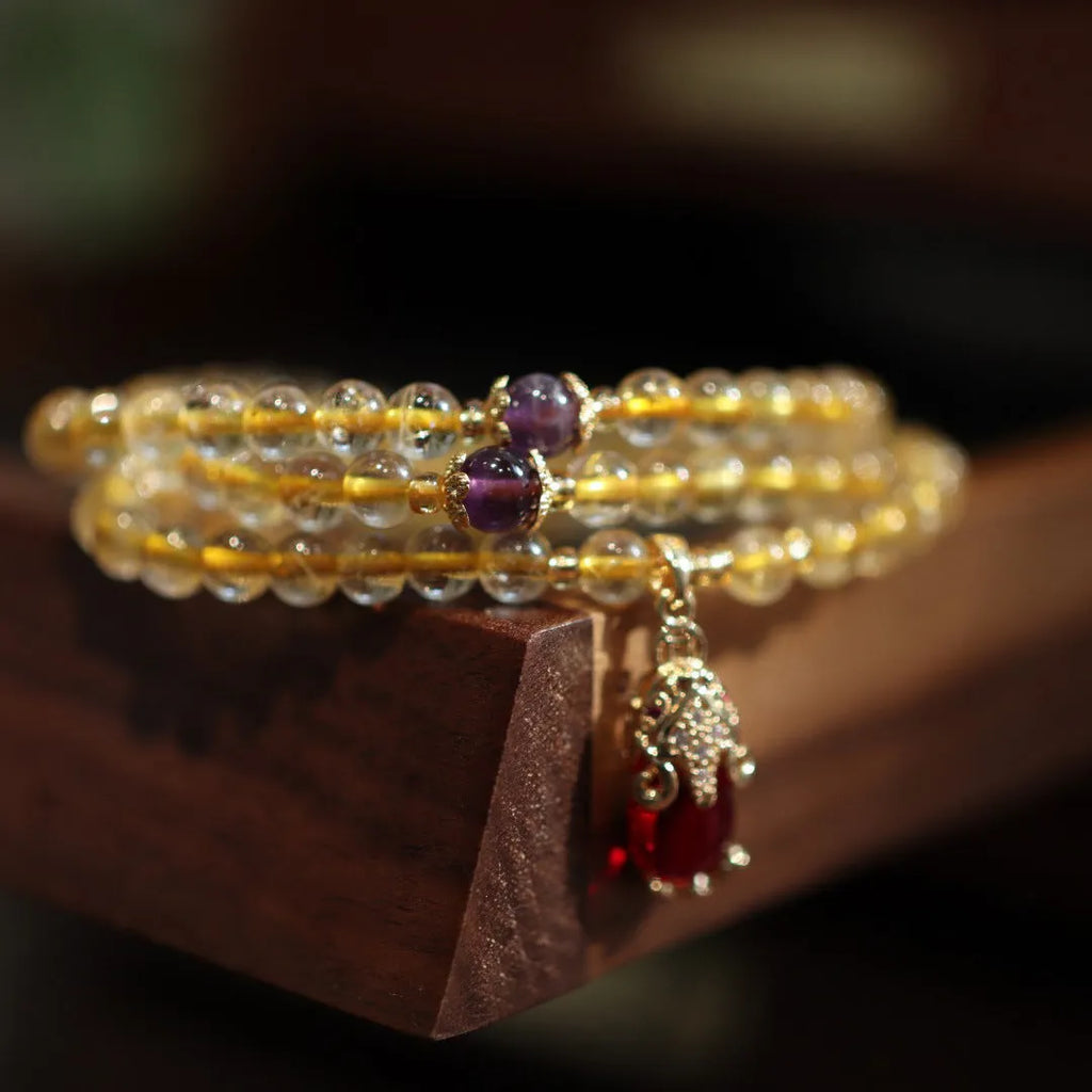 Natural gold rutilated quartz bracelet with three gold circles and a hanging chopstick charm on wrist.