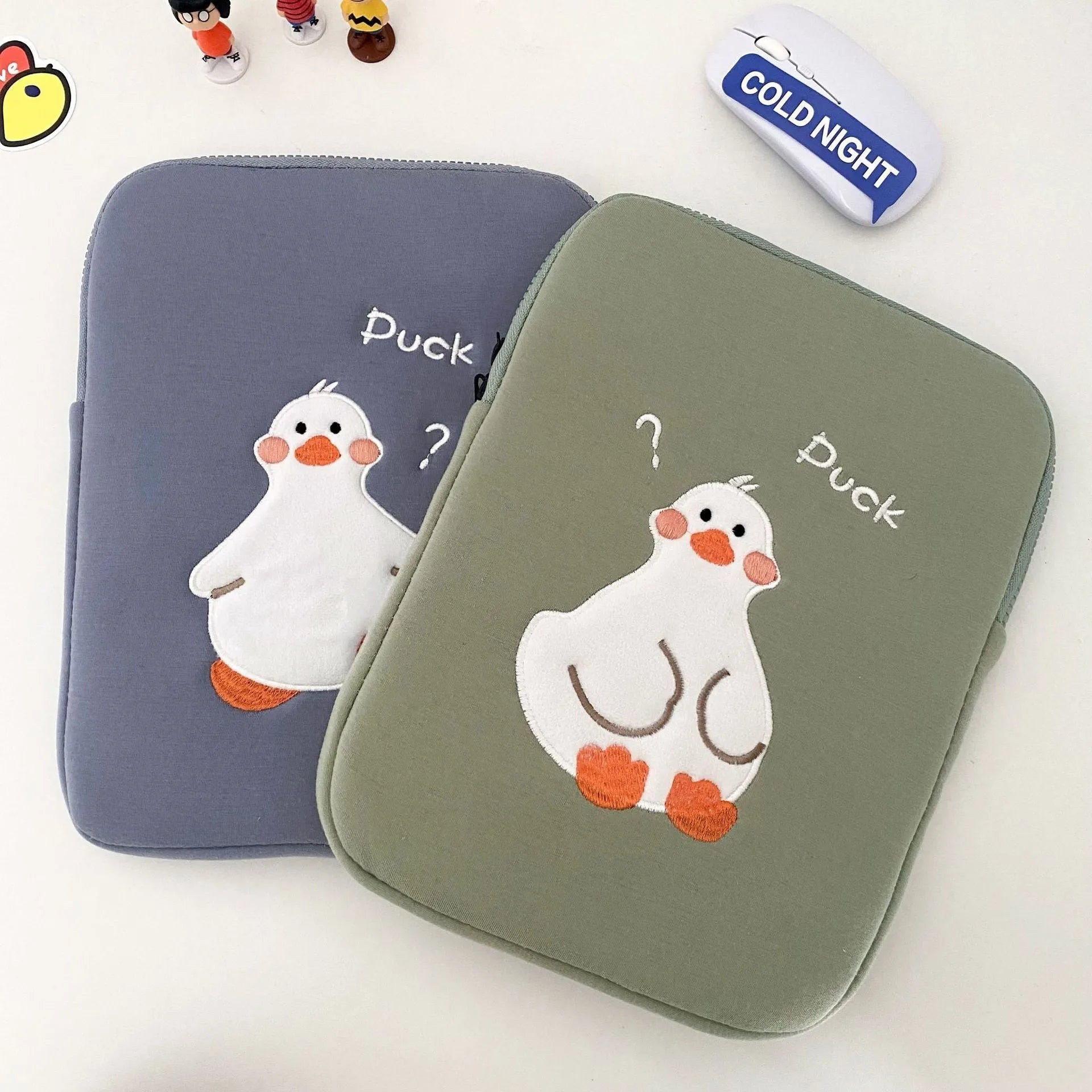 Blue cotton tablet case with embroidered cartoon duck design and a zipper, shown next to a green version.