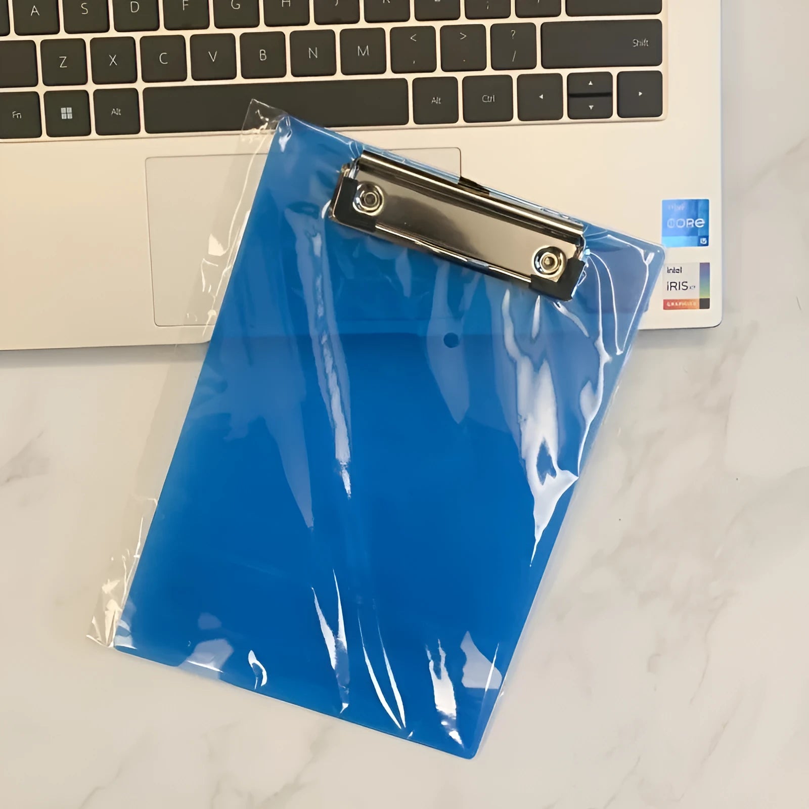 Transparent A4 plate holder with metal clip in blue, holding white paper, on a wooden desk.