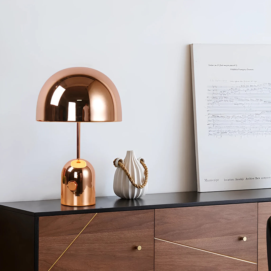 Modern mushroom cap table lamp with a metal base in rose gold finish on a wooden table.