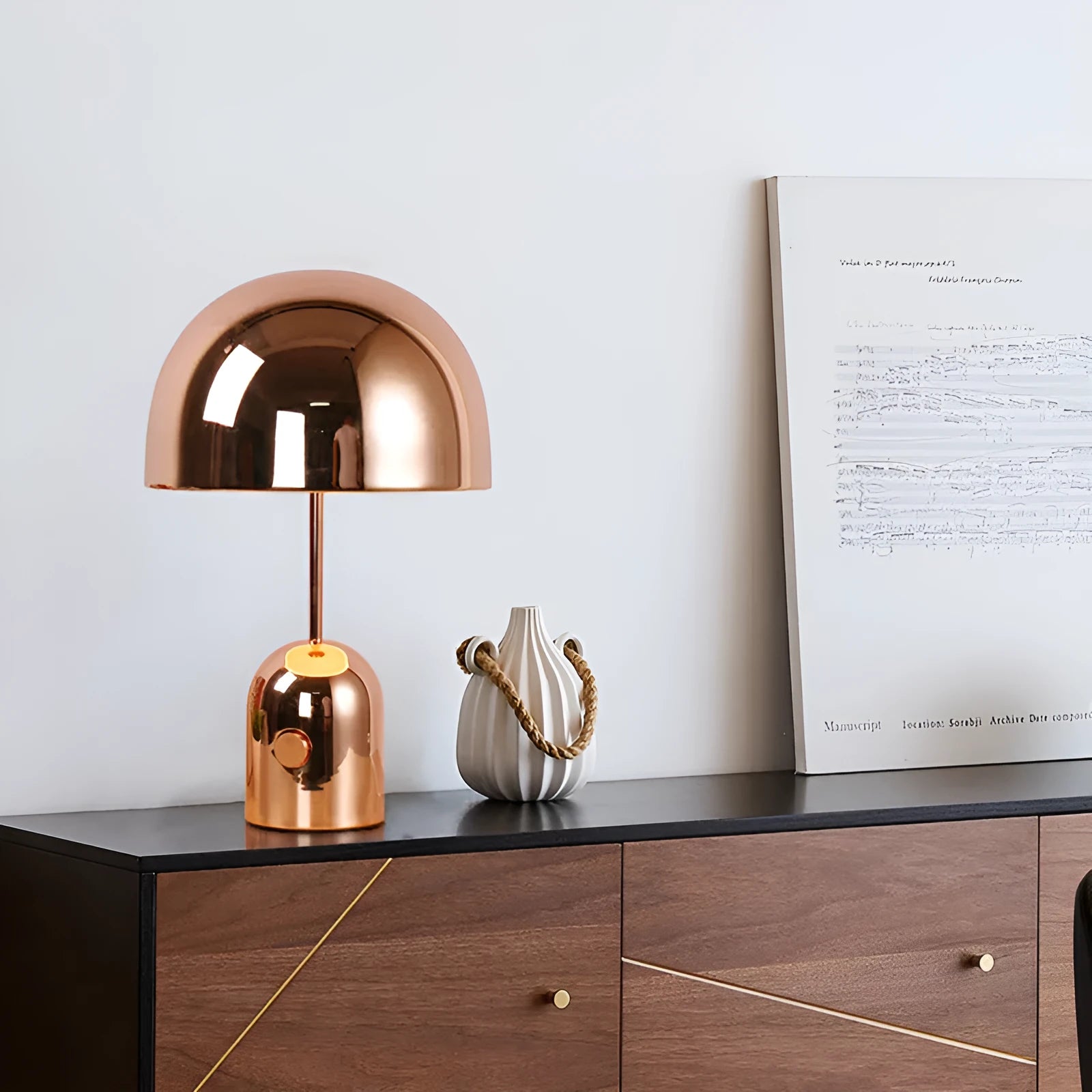 Modern mushroom cap table lamp with a metal base in rose gold finish on a wooden table.