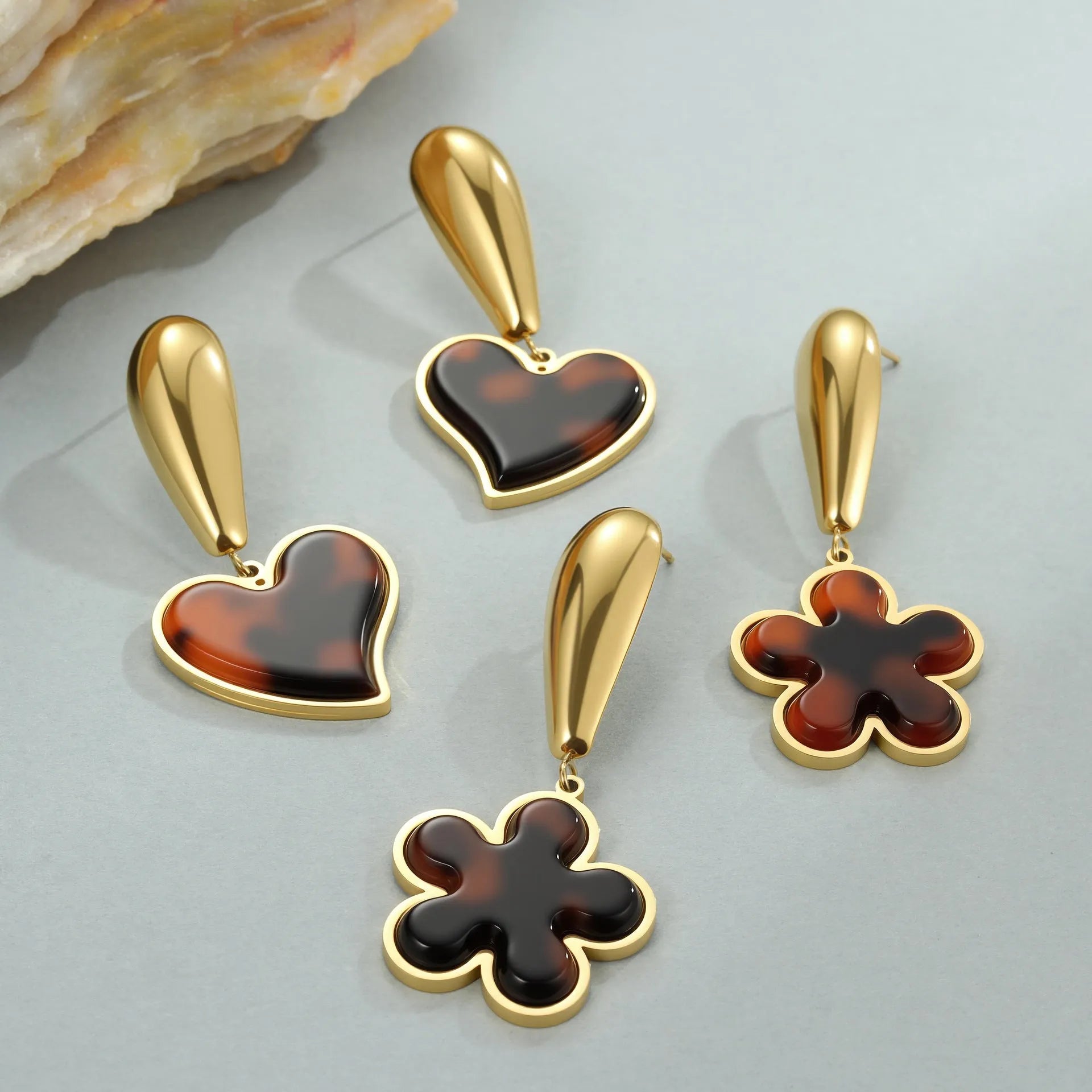 Close up of 18K gold plated stainless steel earrings featuring tortoiseshell resin in heart and flower geometric shapes for women.