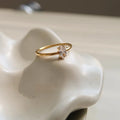 A golden stainless steel ring in a heart shape, shown next to an oval version, on a plain background.