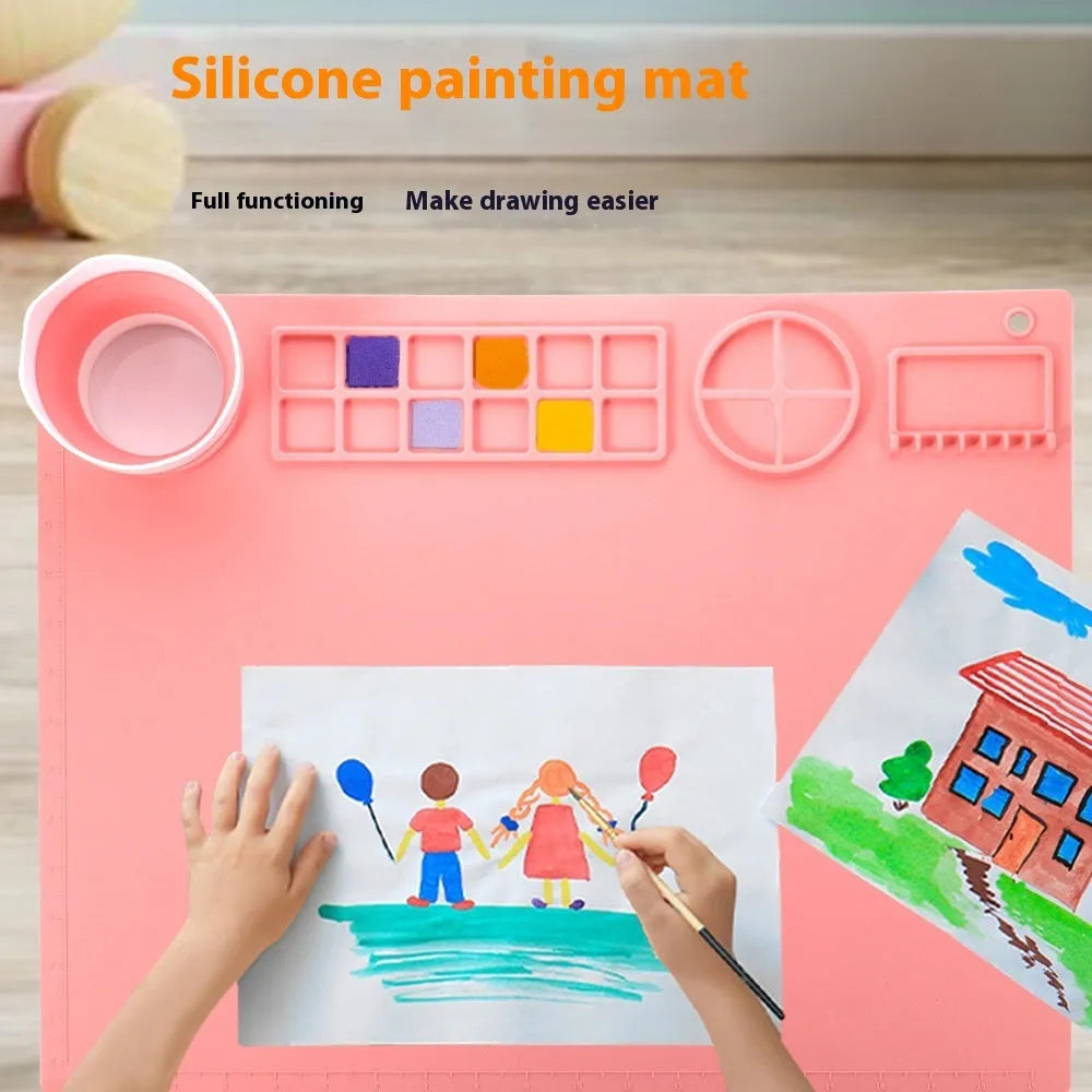 Light blue silicone painting mat with two bowl depressions for water and brushes, placed on a wooden table.