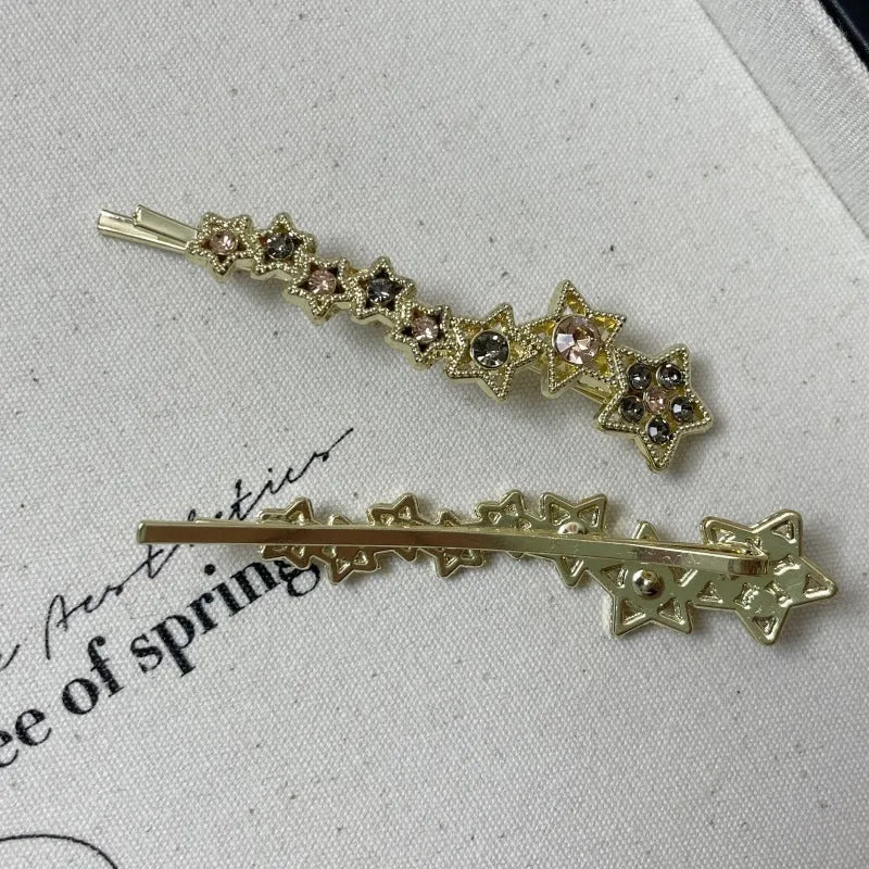 Gold-coloured alloy hair barrette with a side clip, rhinestones, a star, and a word decoration.