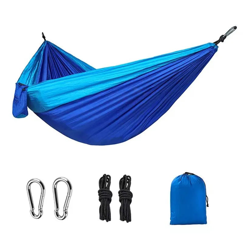 Blue outdoor camping hammock hanging between trees with ropes and carabiners