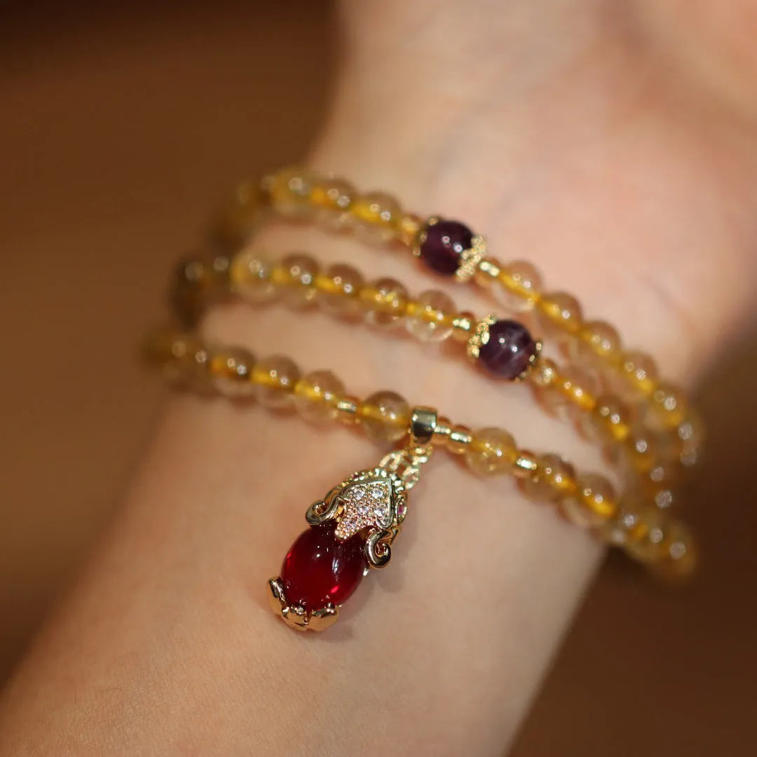 Natural gold rutilated quartz bracelet with three gold circles and a hanging chopstick charm on wrist.