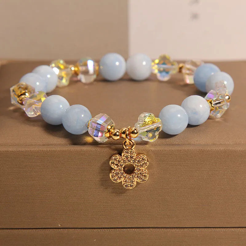 Women's aquamarine crystal bracelet with four-leaf clover charm and pearl details on a wrist.