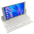 Black folding wireless Bluetooth keyboard shown open next to a tablet demonstrating its compact portable size.