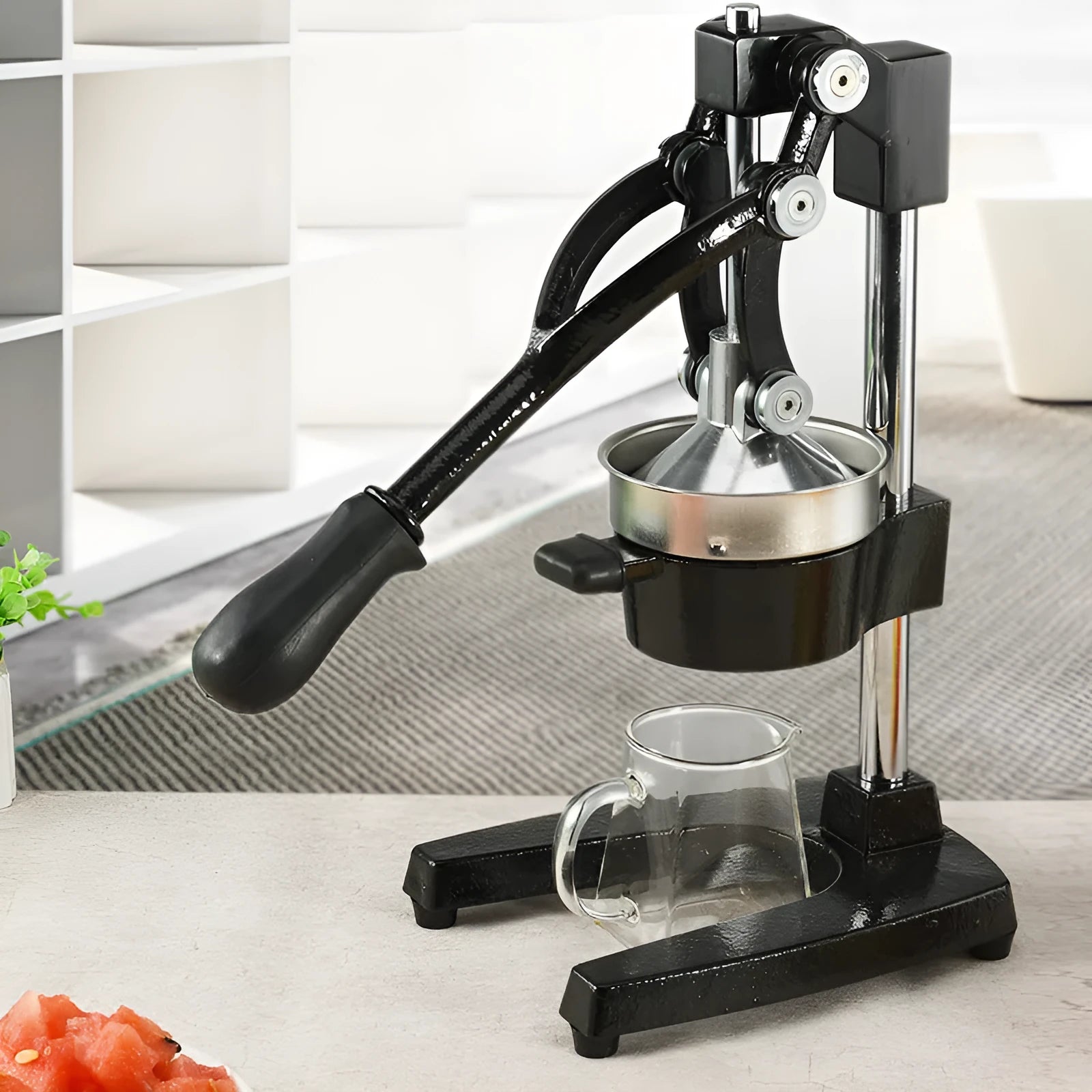 Black manual cast iron citrus juicer with stainless steel strainer on a kitchen counter.
