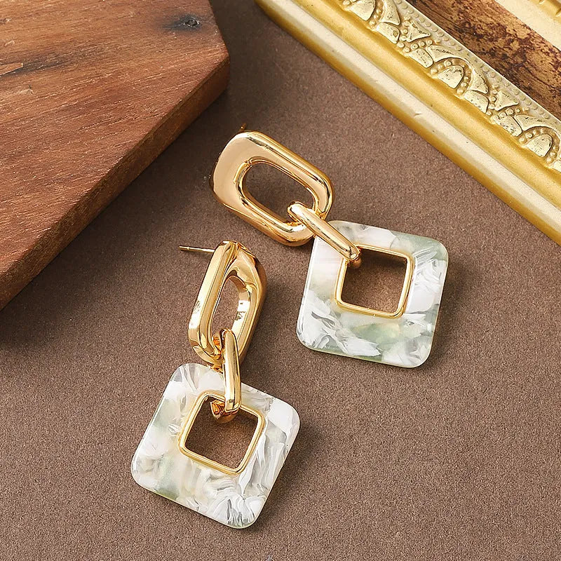 A pair of hollow geometric square earrings with a chamfered pattern, shown in an electroplated finish.