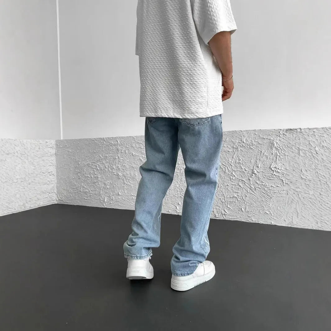Men's blue straight-leg cotton denim trousers with a wide-leg fit and five-pocket design on a neutral background.